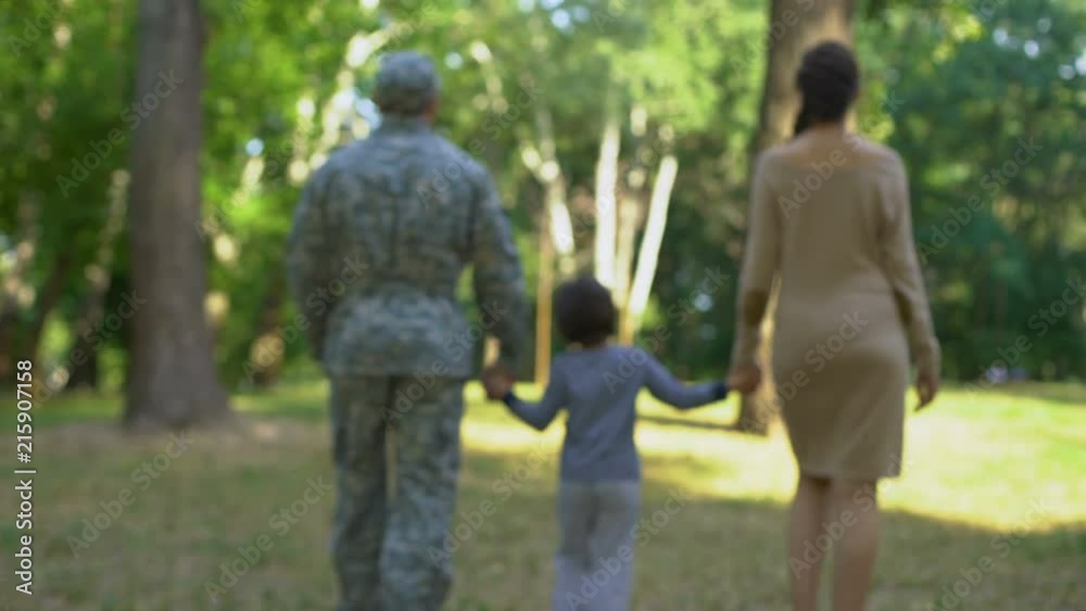 Military father with son and wife walking in park, holding hands, back view Military father with son and wife walking in park, holding hands, back view