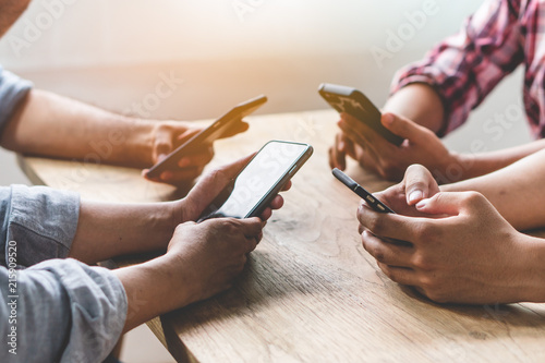 Group of friends playing app games in mobile phone and online together. Hands are holding smartphone circle on the table.