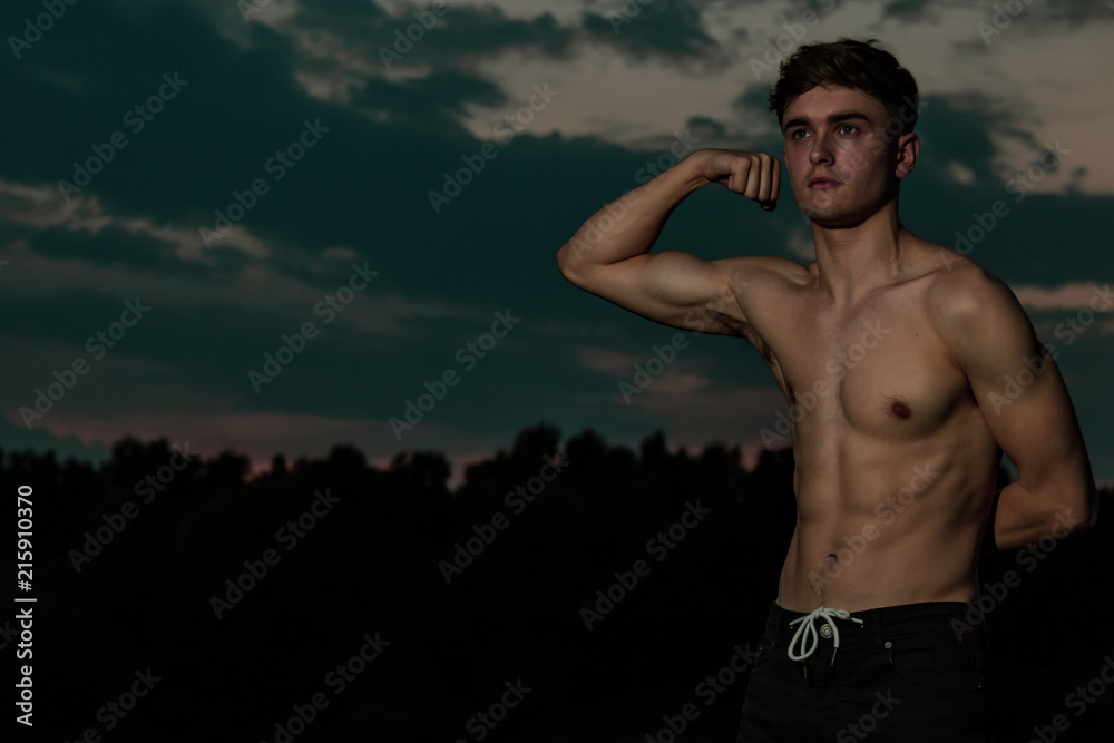 Young adult male flexing his muscles at twilight Young adult male flexing his muscles at twilight