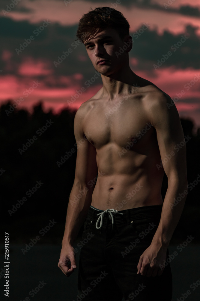 Young adult male flexing his muscles at twilight Young adult male flexing his muscles at twilight