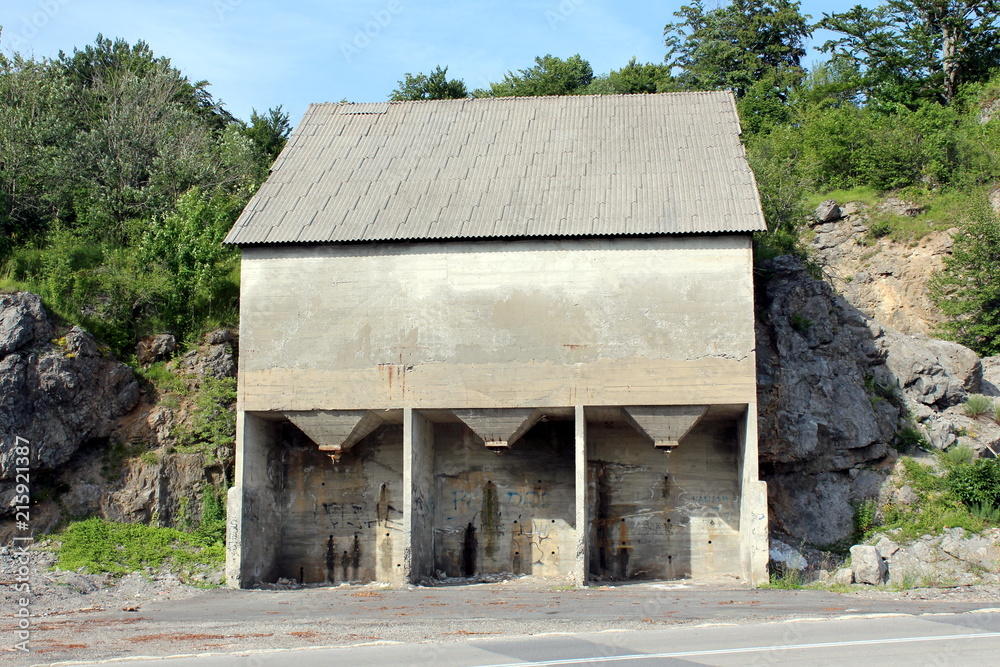 Concrete silos used by winter service for storing sand and salt for road salting during snowy winter days positioned next to paved road for easy access surrounded with massive rocks and forest vegetat Concrete silos used by winter service for storing sand and salt for road salting during snowy winter days positioned next to paved road for easy access surrounded with massive rocks and forest vegetat