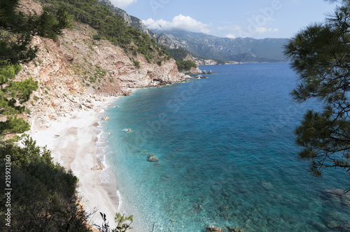 Fototapeta Naklejka Na Ścianę i Meble -  Colorful landscape of the uninhabited Mediterranean coast of Turkey; Sea bay with a beach and rocky capes overgrown with forest; Sea, mountains, woods and blue sky on the sunny summer day