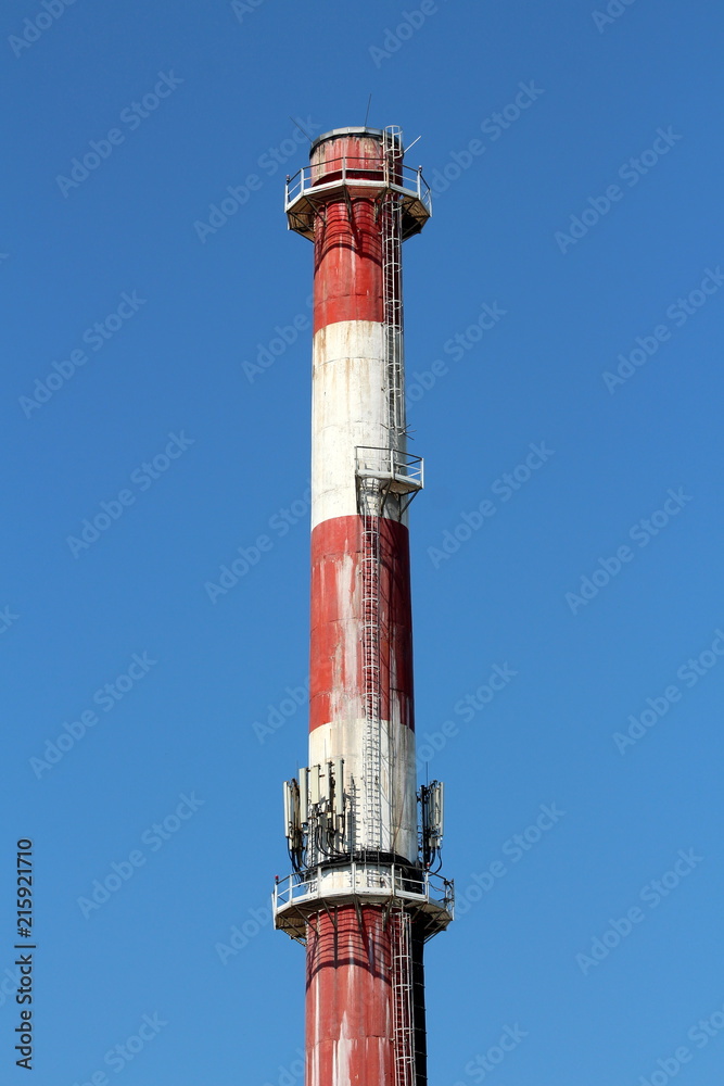 Top of high industrial red and white chimney with multiple cell phone antennas and metal stairs on clear blue sky background Top of high industrial red and white chimney with multiple cell phone antennas and metal stairs on clear blue sky background