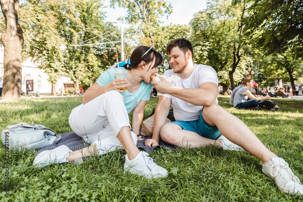 couple sitting on green grass eating burgers drinking smoothie couple sitting on green grass eating burgers drinking smoothie