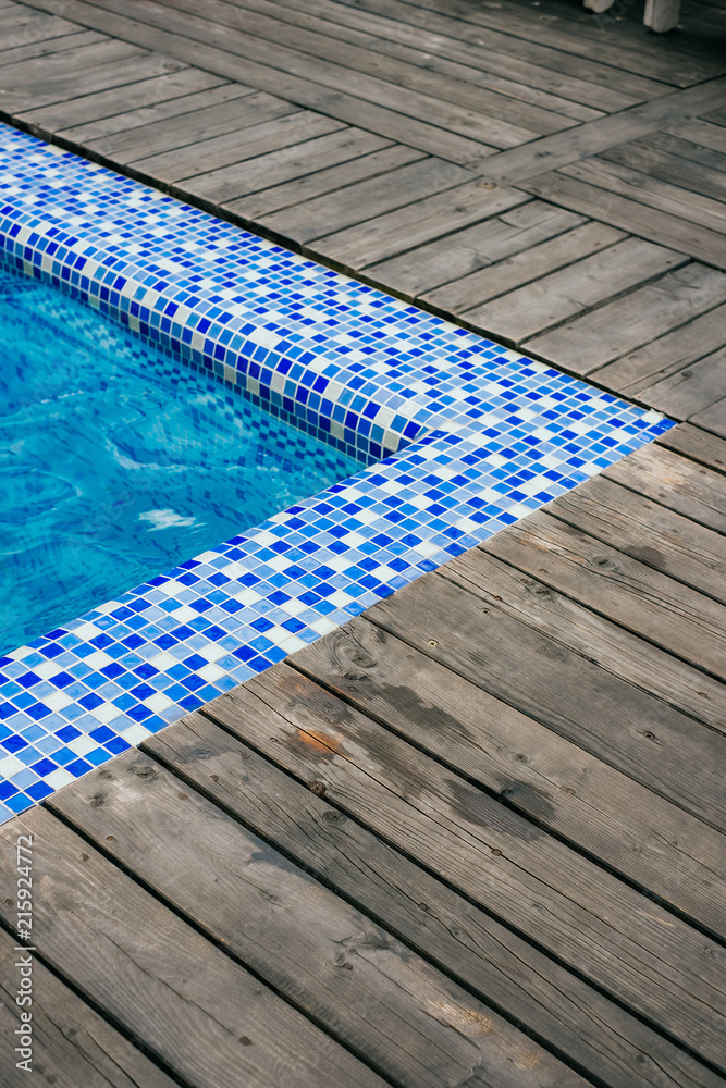 Bright blue swimming pool corner and wooden deck at hotel.