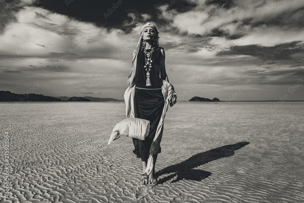 Fototapeta premium beautiful young stylish woman walking on low tide at sunset. black and white. fashion concept