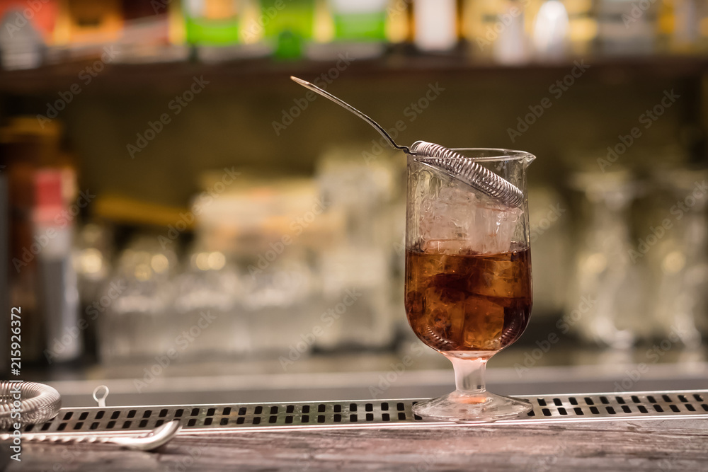 A glass with alcoholic cocktail standing on bar counter. Mixing alcohol drink process. Modern trends in club and bar industry. Selective focus on the glass. A glass with alcoholic cocktail standing on bar counter. Mixing alcohol drink process. Modern trends in club and bar industry. Selective focus on the glass.