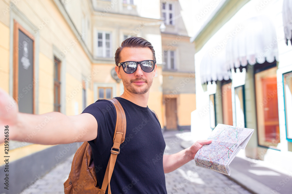 Fototapeta premium Man tourist with a city map and backpack in Europe street. Caucasian boy looking with map of European city.