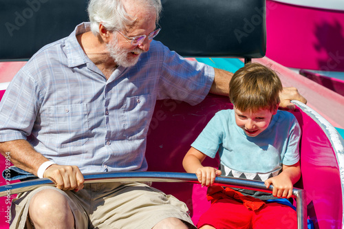 An Elderly Man and His Young Grandson Ride on a Spinning Carnival Ride the Man is Looking at the Little Boy
