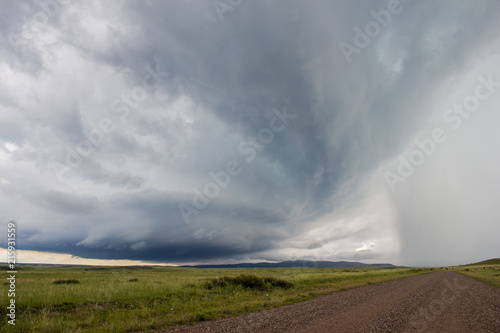 Looking down a gravel road at a supercell thunderstorm approaching with mountains on the horizon.