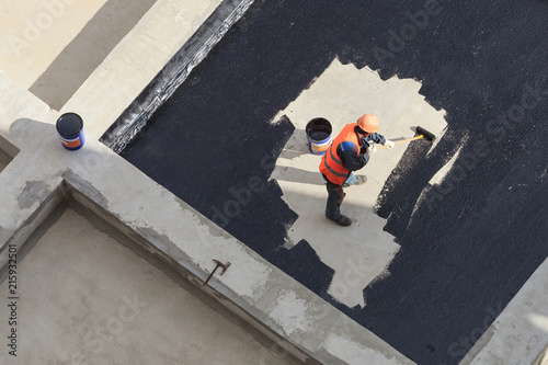 The worker in overalls applies an insulation coating on the concrete surface. View from above. photo