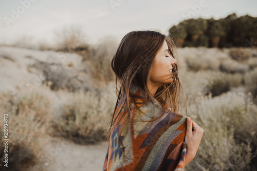 Back side of boho woman with windy hair in the desert nature, turning her head and smiling .  Artistic photo of young hipster traveler girl in gypsy look, in Coachella Valley in a desert vall photo