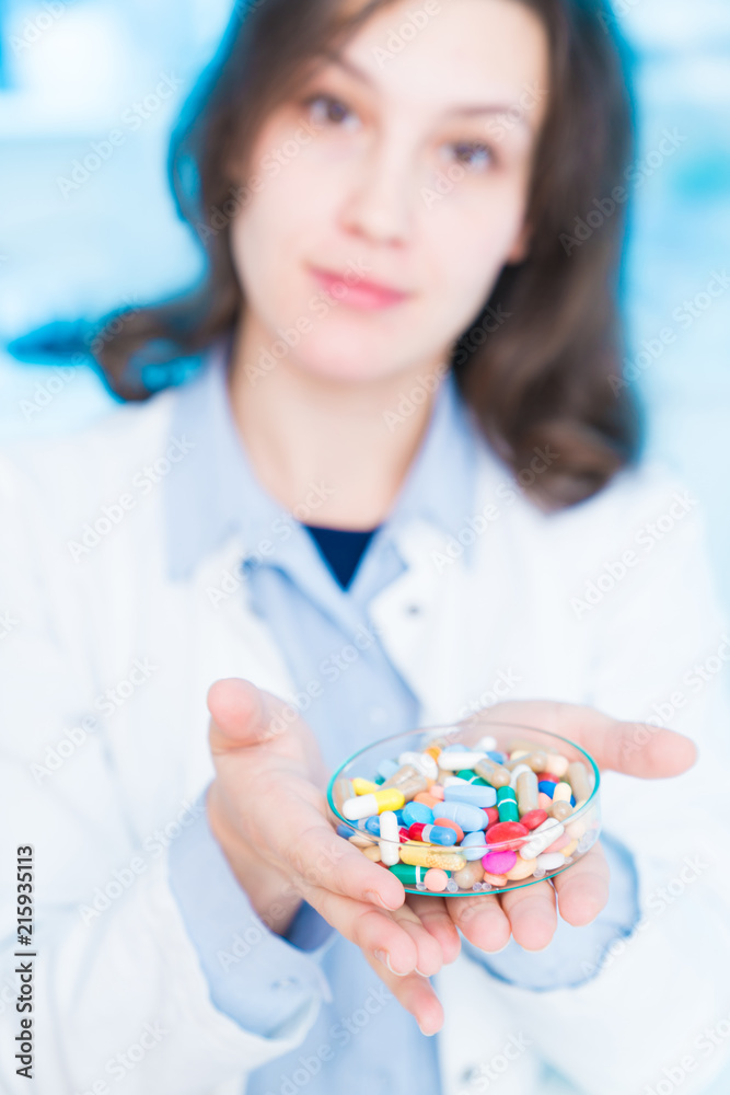 young woman doctor smiling and holding one pill over blue background