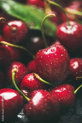 Fresh sweet cherry texture, wallpaper and background. Wet sweet cherries with leaves on dark background, selective focus, close-up, vertical composition. Summer food or local market produce concept