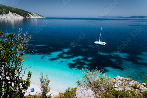Fteri beach, Cephalonia Kefalonia, Greece. White catamaran yacht on clear transparent blue azure sea water surface. Paradise beach
