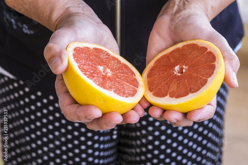 mature woman hands take a grapefruit. colors and offer concept for healthy life and lifestyle. seasonal fresh fruit cutted in the middle. half measure
