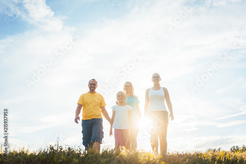 Family walking in sunset over a summer meadow, backlit scene