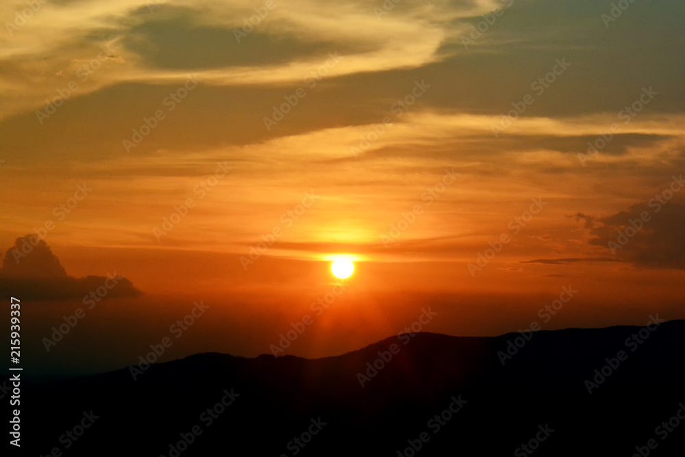 sunset sunrise in orange colors and sun over dark mountain silhouette.