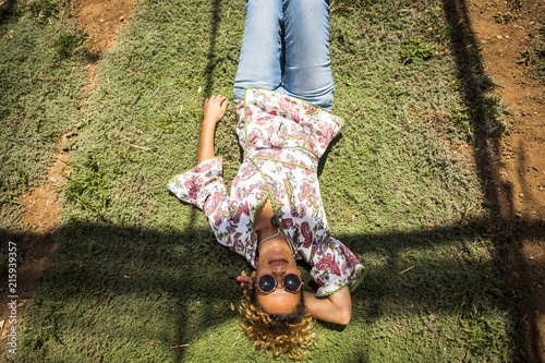aerial point of view for pretty woman smile and rest laying down on a timo grass. hippy and fashion clothes with jeans. sunglasses and relaxed leisure activity outdoor enjoying the nature photo