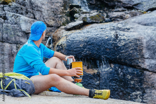 Hiker man traveler in blue sportswear preparing hot drink with a portable gas burner in Norway mountains. photo