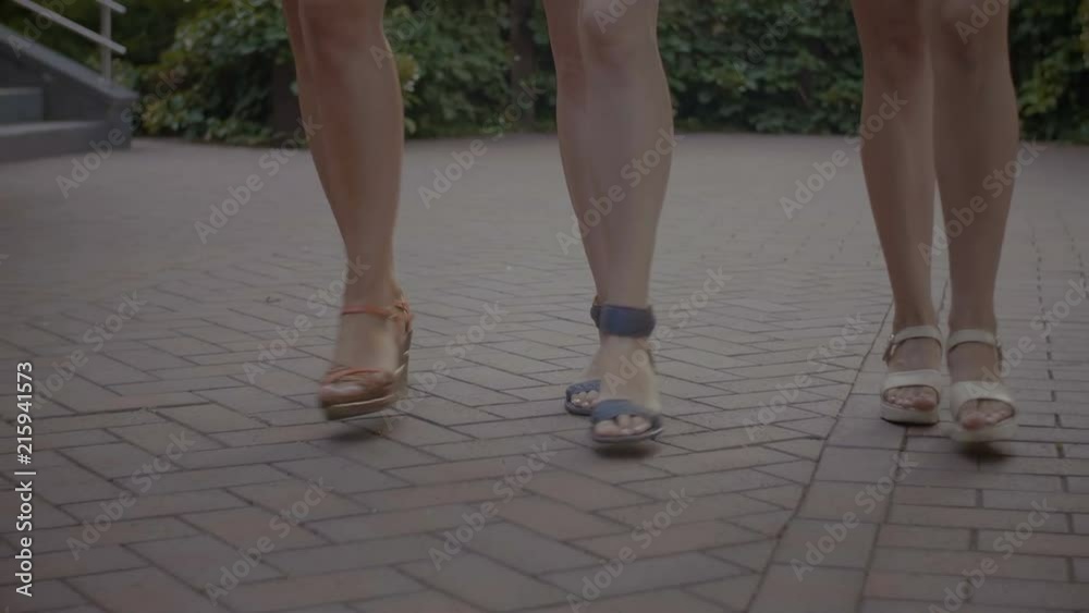 Closeup of slim beautiful female legs in stylish shoes walking along park alley during summer promenade outdoors. Low angle view. Elegant women taking a stroll in summer park. Slow motion. Closeup of slim beautiful female legs in stylish shoes walking along park alley during summer promenade outdoors. Low angle view. Elegant women taking a stroll in summer park. Slow motion.