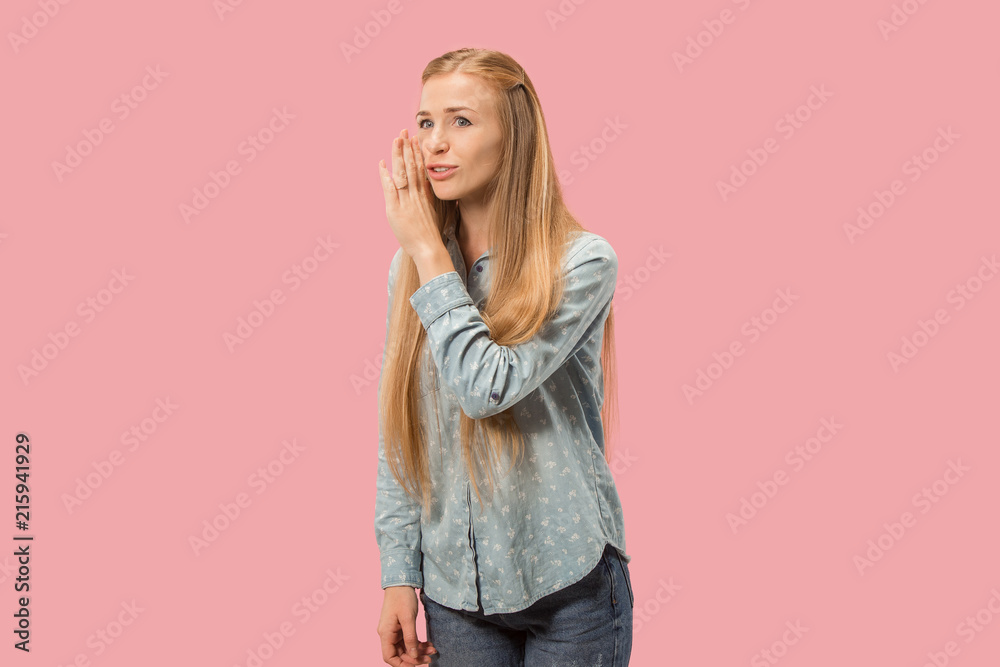 The young woman whispering a secret behind her hand over pink background The young woman whispering a secret behind her hand over pink background