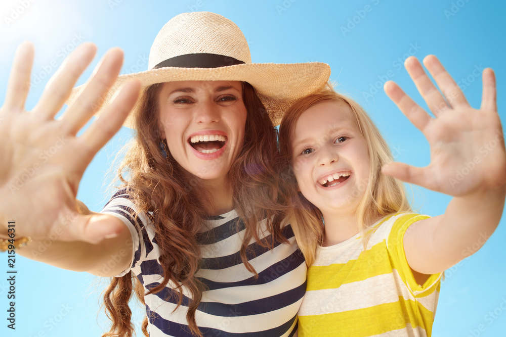 happy young mother and daughter greeting against blue sky