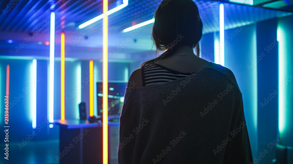 Back View Shot of the Beautiful Professional Gamer Girl Looking at Her Room in Retro Neon Lights with Her Personal Computer. Casual Cute Geek wearing Glasses. Back View Shot of the Beautiful Professional Gamer Girl Looking at Her Room in Retro Neon Lights with Her Personal Computer. Casual Cute Geek wearing Glasses.