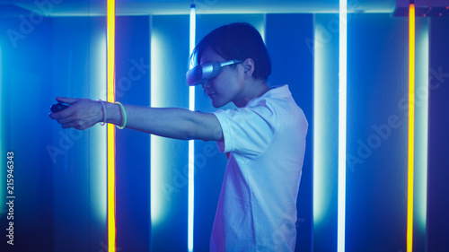 East Asian Pro Gamer Wearing Virtual Reality Headset Plays Online Video Game Shooter using Joysticks / Controllers as Shotgun / Gun. Cool Retro Neon Colors in the Room.