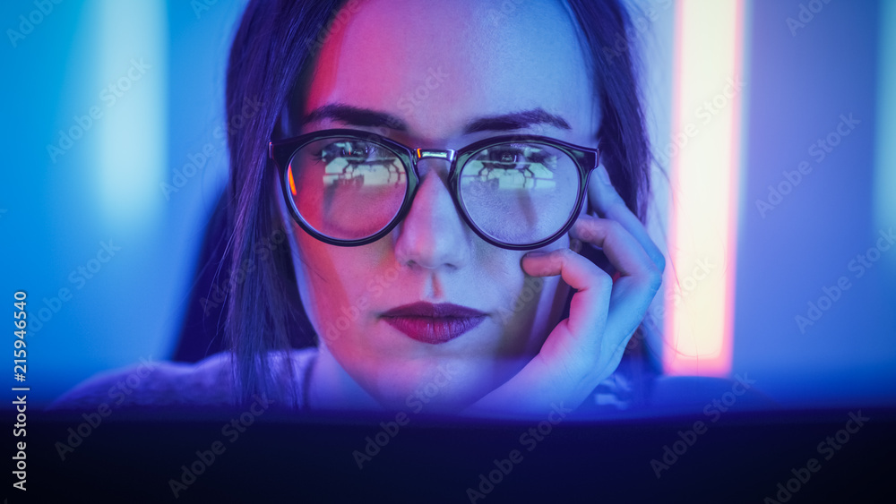 Portrait of the Beautiful Young Girl Sitting Before Computer Screen, Browsing in Internet, Playing Online Games, Streaming. Cute Girls Wearing Glasses in the Cool Retro Neon Lit Room. Portrait of the Beautiful Young Girl Sitting Before Computer Screen, Browsing in Internet, Playing Online Games, Streaming. Cute Girls Wearing Glasses in the Cool Retro Neon Lit Room.