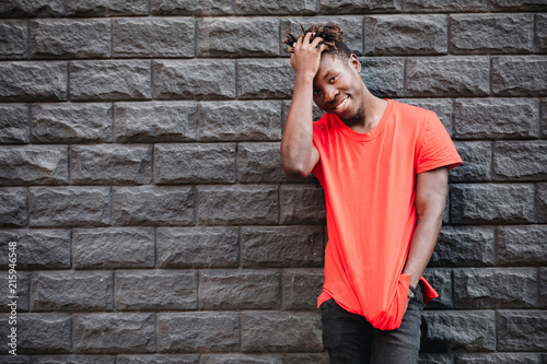 African man model smiling in red t-shirt against brick wall with facepalm