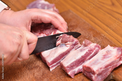 Cutting pork meat with a black knife, close-up, on a cutting board. Pork meat ribs