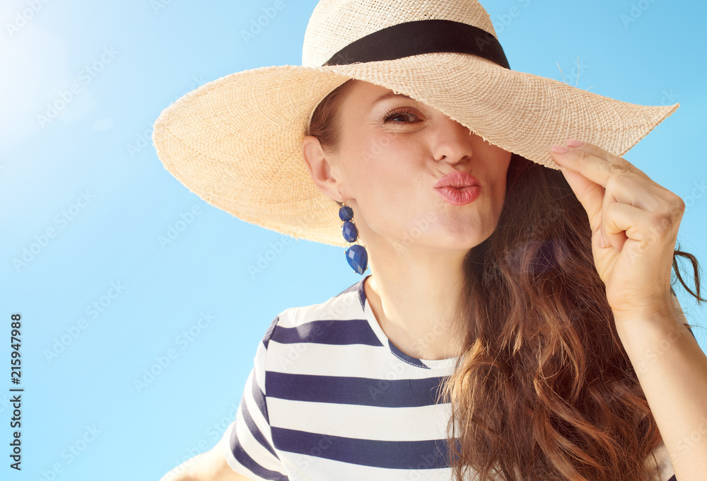 cheerful modern woman against blue sky playing with straw hat
