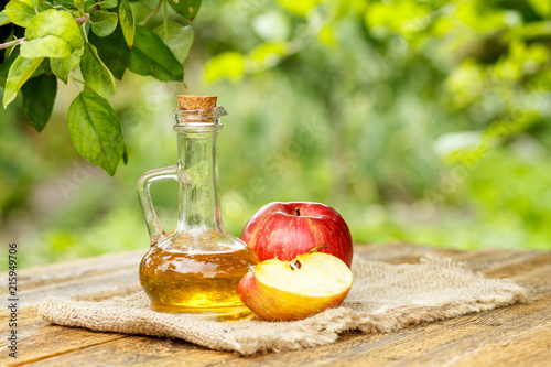 Apple vinegar in glass bottle and fresh red apples on wooden boa