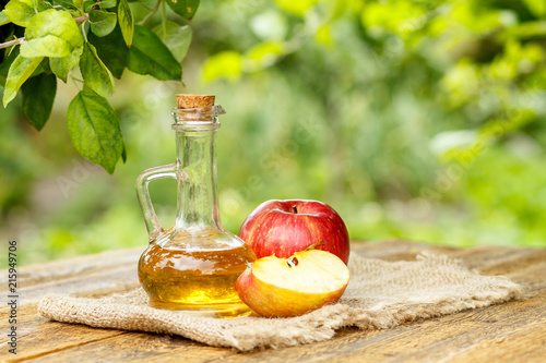 Apple vinegar in glass bottle and fresh red apples on wooden boa photo