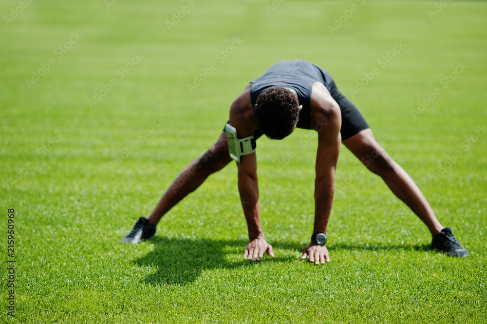 African american male athlete in sportswear doing stretching exercise at stadium.