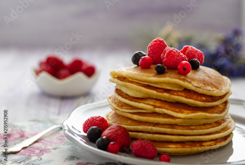 Stack of gold pancakes with berries and honey on wooden background