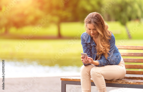 Young woman sitting on bench and use her phone in park photo