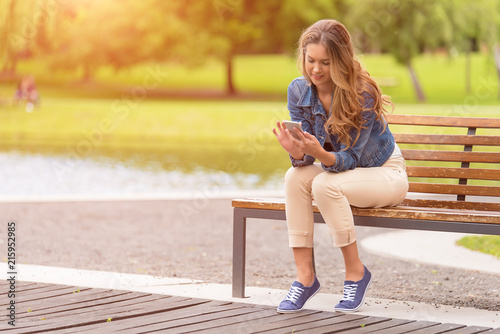 Young woman sitting on bench and use her phone in park