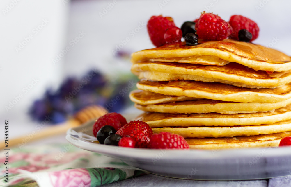 Stack of gold pancakes with berries and honey on wooden background