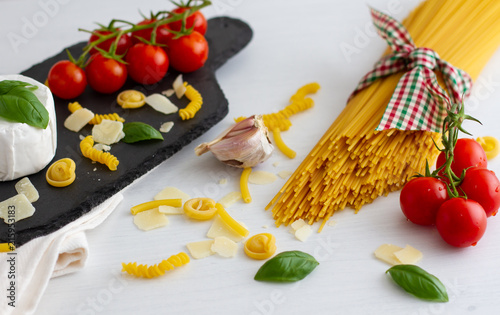 Bunch of uncooked long italian spaghetti tied with a cord in the colours of the national flag on white background. Served with cherry tomatoes basil chesse.Culinary background