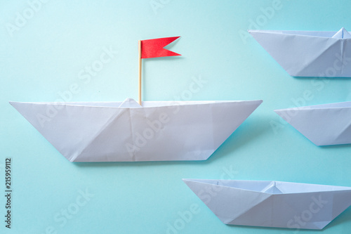 Leadership concept using  paper ship with red flag on blue background