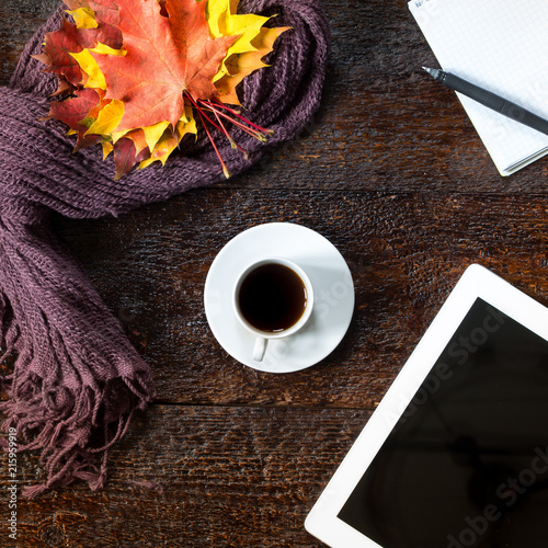 Still life of cup of coffee, scarf,autumn leaves, notepad, pen and tablet on brown wooden background