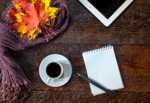 Still life of cup of coffee, scarf,autumn leaves, notepad, pen and tablet on brown wooden background