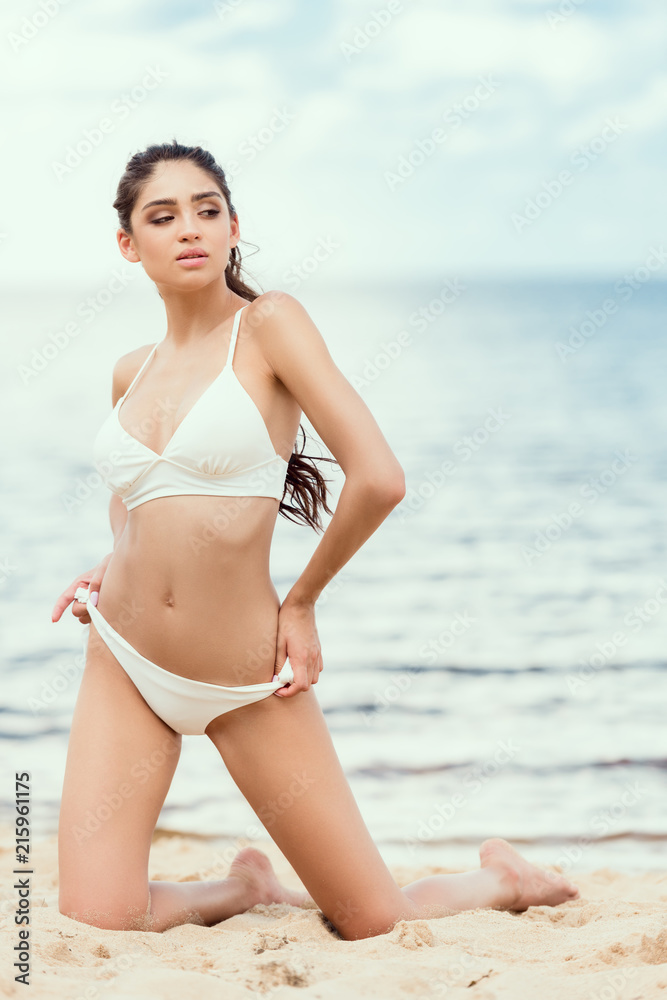 brunette woman in white swimsuit relaxing on beach at sea