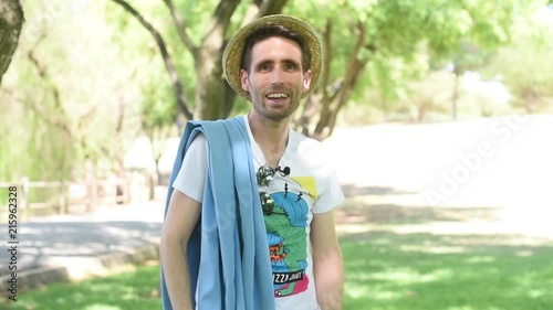 Hombre joven vestido con ropa veraniega, con sombrero y toalla, bailando divertido y riéndose.