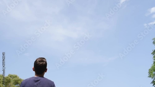 Hombre con camiseta azul de espaldas bajo dielo azul despejado al aire libre en la naturaleza.