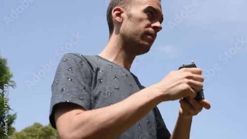 Fotógrafo con camiseta de pájaros haciendo fotos o tomando imágenes en movimiento con una cámara antigua de película con una manivela. Imagen al aire libre en el campo bajo un cielo azul despejado.
