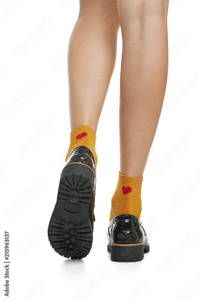 Cropped back view of beautiful woman's legs in orange socks with red hearts  and patent leather shoes with ribbed soles, isolated over a white  background. Fashionable legwear and footwear for ladies. Stock