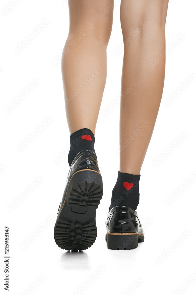 Cropped back view of beautiful woman's legs in black socks with red hearts  and patent leather shoes with ribbed soles, isolated over a white  background. Fashionable legwear and footwear for ladies. Stock